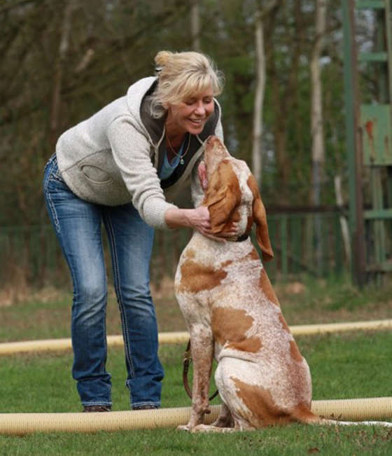 Susa Gülzow beugt sich auf dem Trainingsplatz zu einem orange-weißen Hund, der aufmerksam zu ihr aufschaut